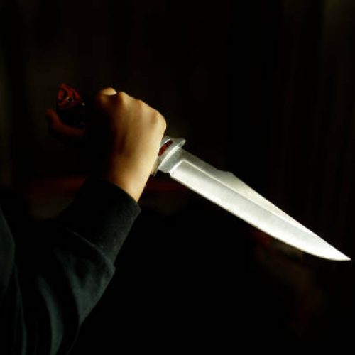 Close-up of a hand holding a large knife in a dark room. Concept of crime and violence.