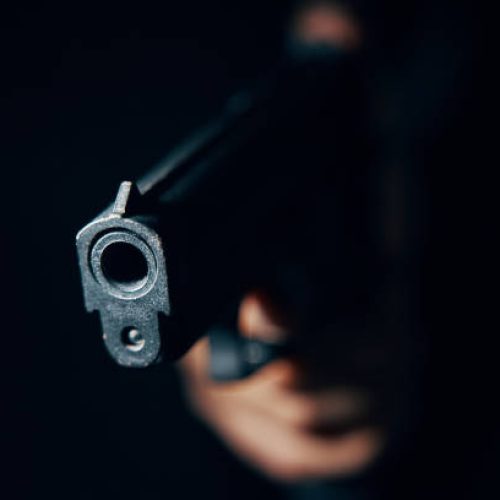 Gun pointed at camera in close-up. Pistol in hand in dark. Criminal with dangerous firearm. Attack or defense.